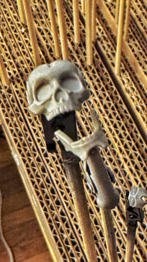 grainy low-light photo of a very small plastic skull and separate jaw clamped to a DIY cardboard block